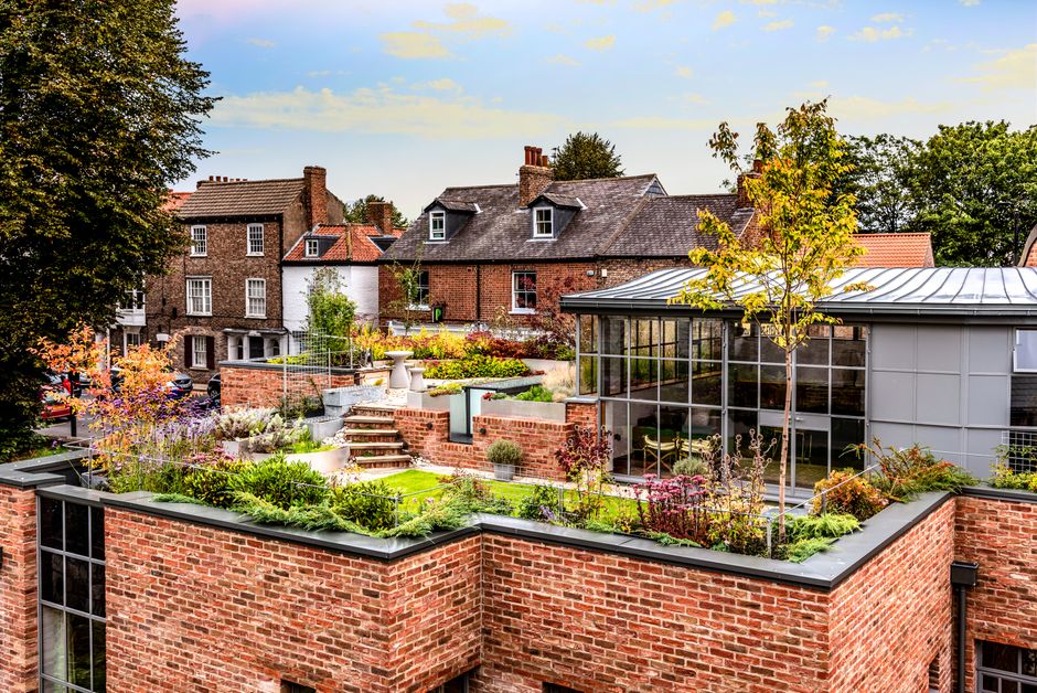 A rooftop terrace in Camden Town NW1 featuring a paved pathway leading towards a small classical pavilion with a domed roof and arched opening. The terrace is decorated with numerous rectangular woode