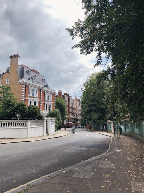 A wide street scene in a residential area of Chelsea SW3, featuring a tall, historic brick building with ornate architectural details, including a mansard roof with dormer windows, decorative brickwor